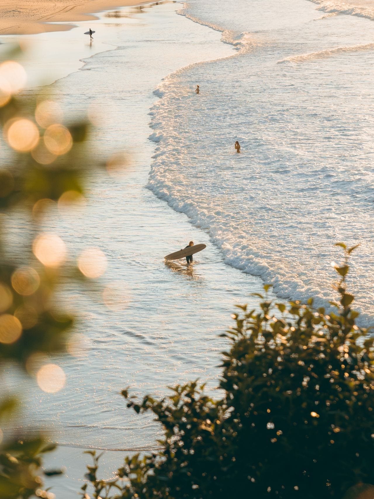 Morning light on the water, a surfer wading out through the shallows