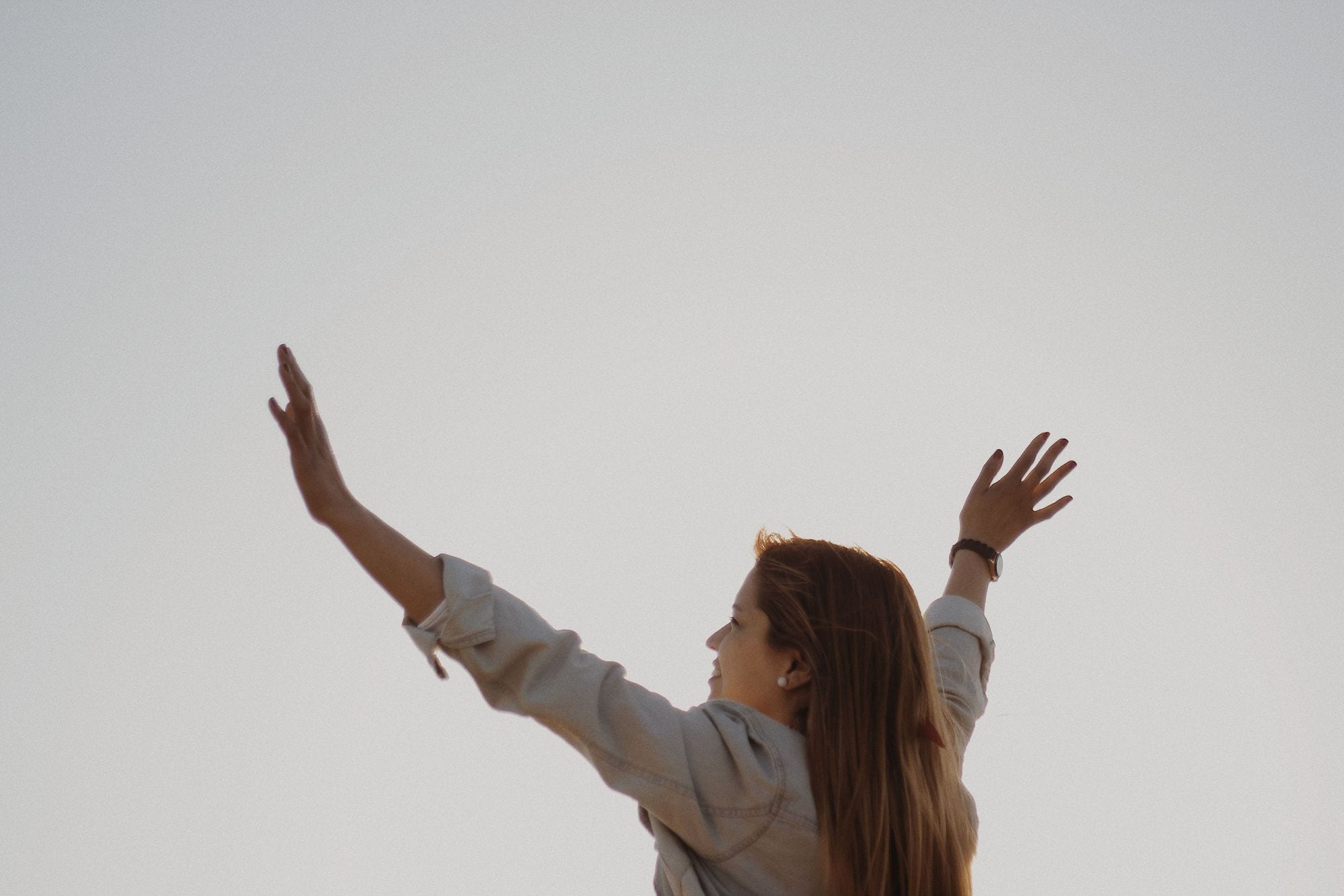A woman with her arms raised against a pale, misty sky
