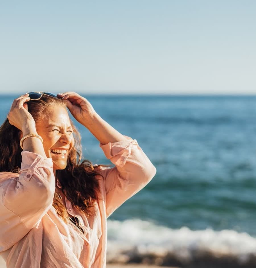 A woman laughing on the shoreline, hands in her hair